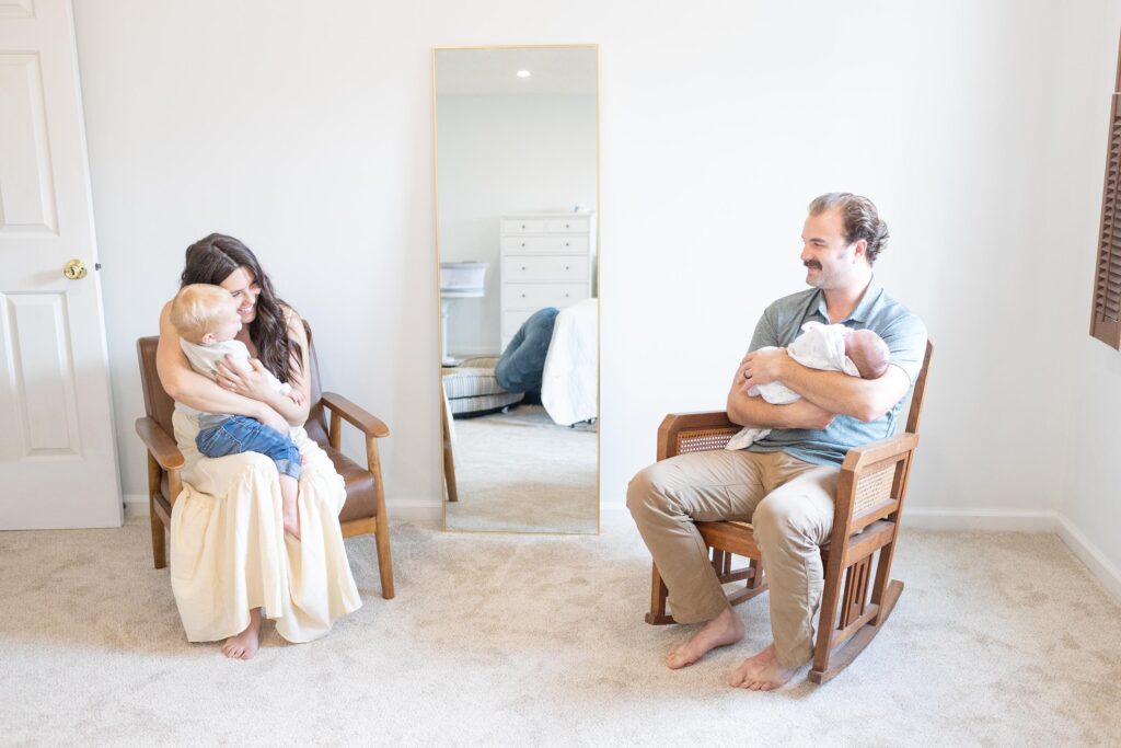 Mom and Dad sitting on chairs during an in-home session each holding one of their two young children by Mary Eleanor Photography.