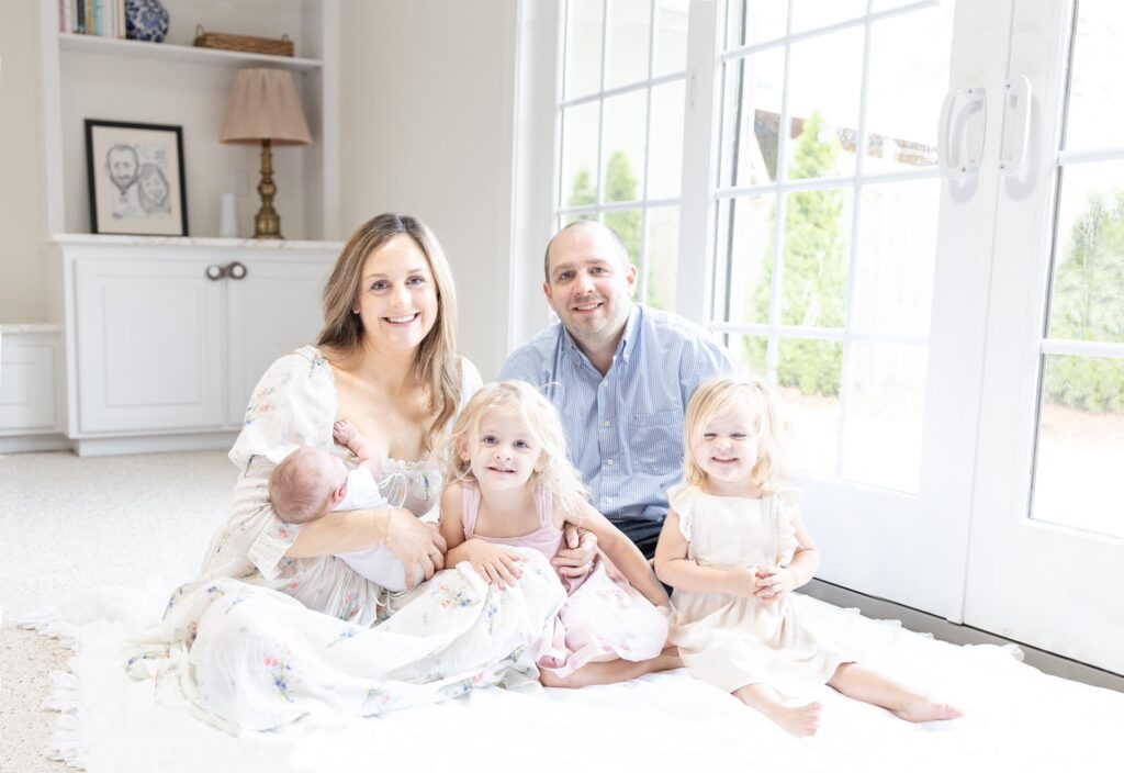 Photo of a young family Mom wearing a Doen Painted Blooms dress, sitting on the floor looking at the camera during an in-home session by Mary Eleanor Photography.