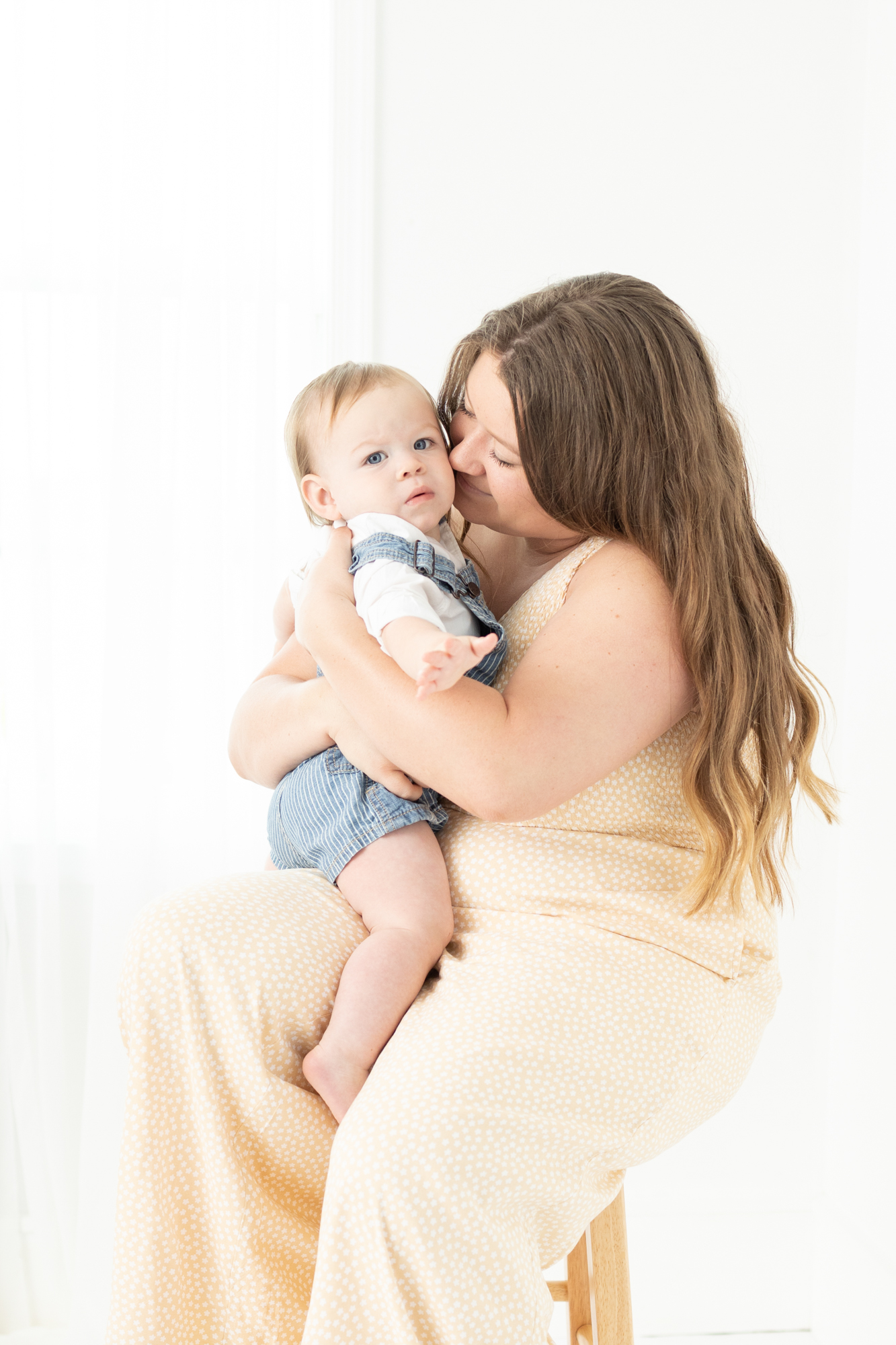 A happy new mom snuggles her baby in her lap on a stool in a studio before visiting Ice Cream Shops in Virginia Beach