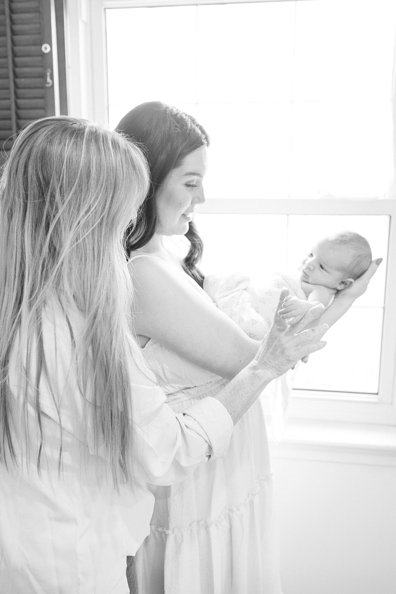 A new mom holds her newborn in a window as it holds grandma's finger after visiting baby stores in virginia beach