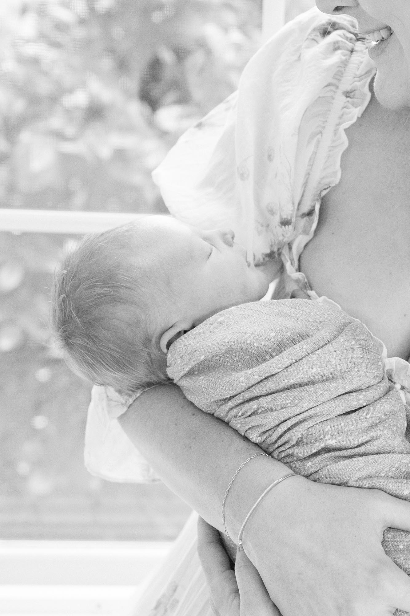 A newborn baby sleeps in a swaddle in mom's arms in a window in black and white after visiting baby stores in virginia beach
