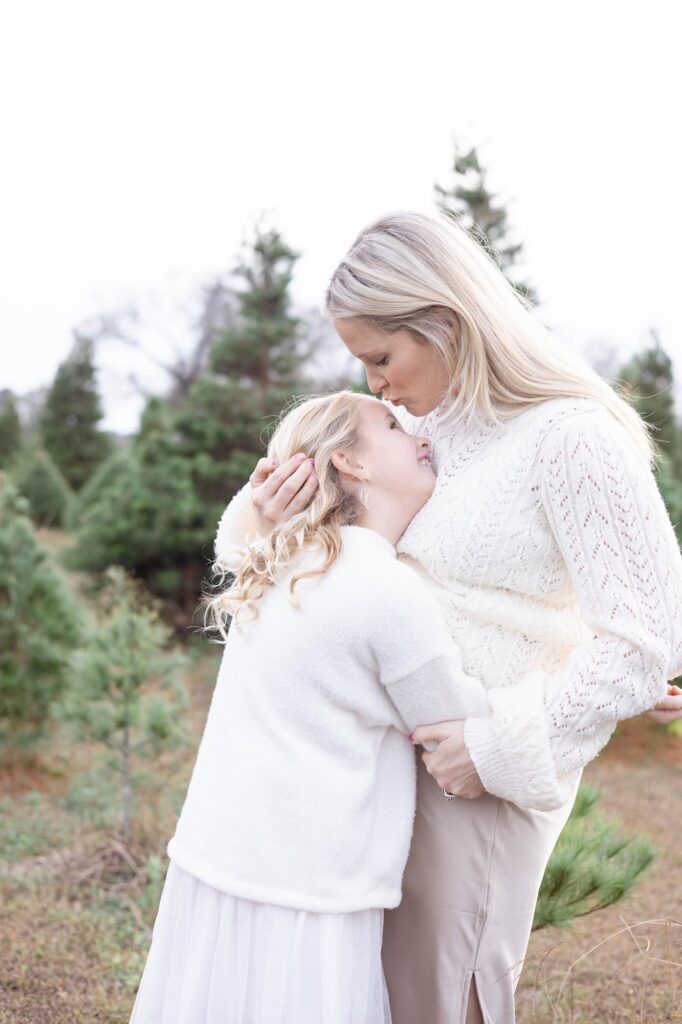 A mother hugs her daughter close while standing in a Christmas Tree Farm in Virginia Beach by Mary Eleanor Photography.