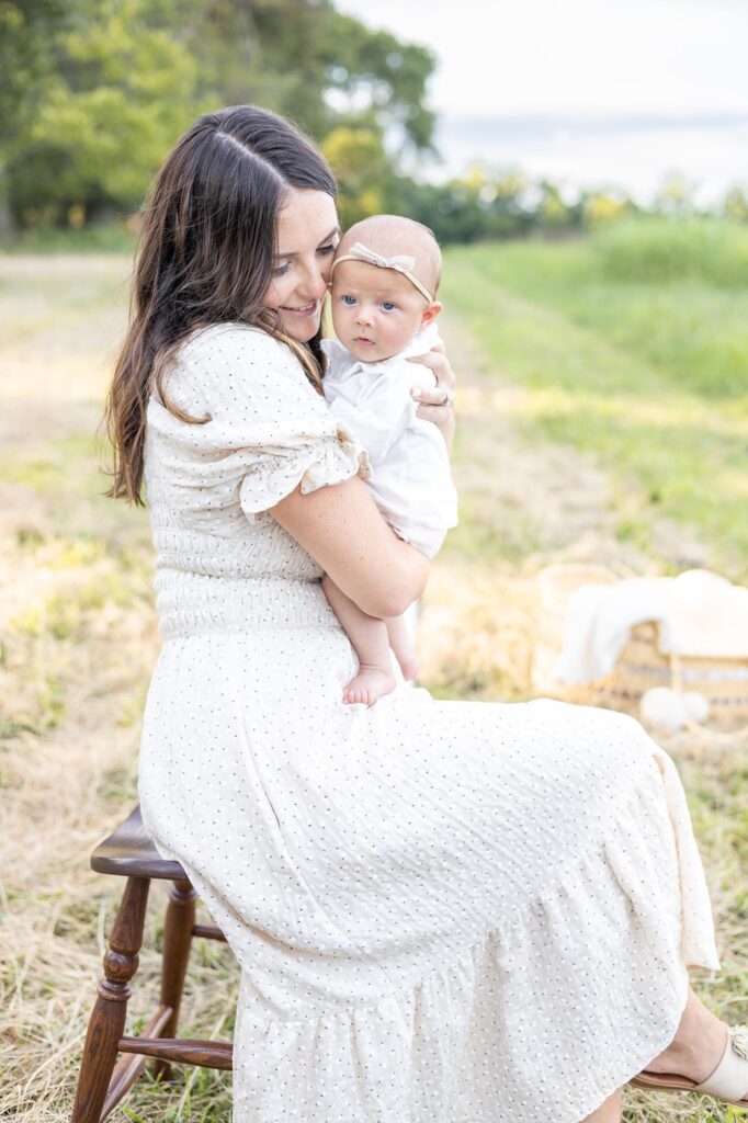 A mom where a cream dress with small flowers snuggles her infant close while resting on a stool during Fall Family Photos by Mary Eleanor Photography.