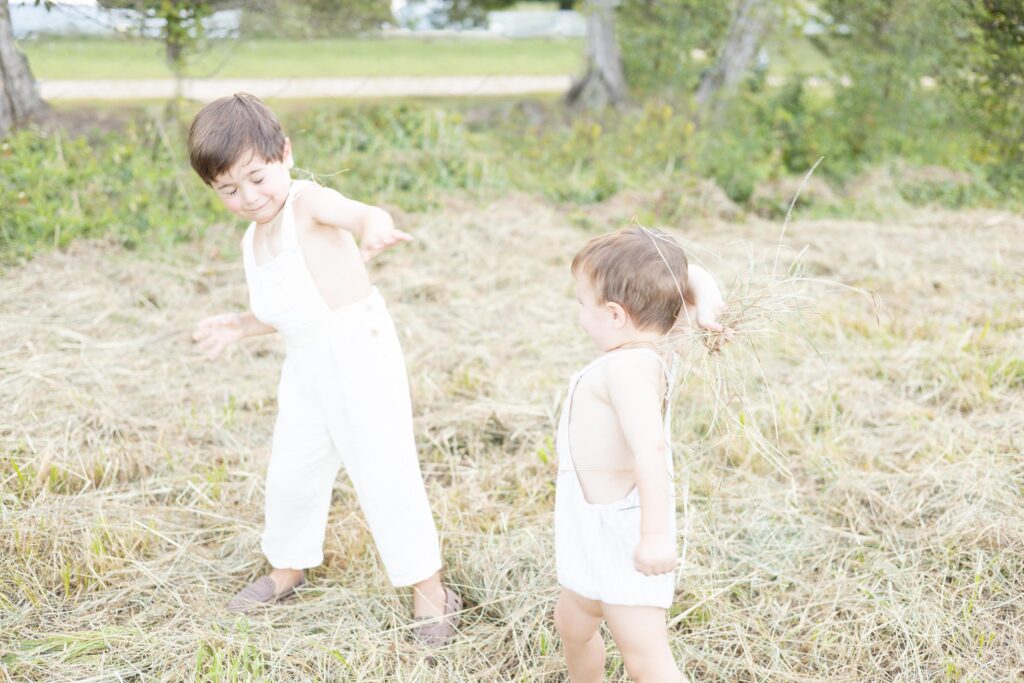 Two toddler aged brothers play together throwing hay during Fall Family Activities in Virginia Beach.
