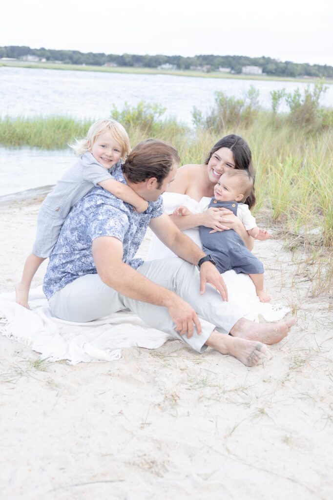 A young Family laugh with each other playing on the beach during a family vacation at a family friendly hotel in Virginia Beach by Mary Eleanor Photography.