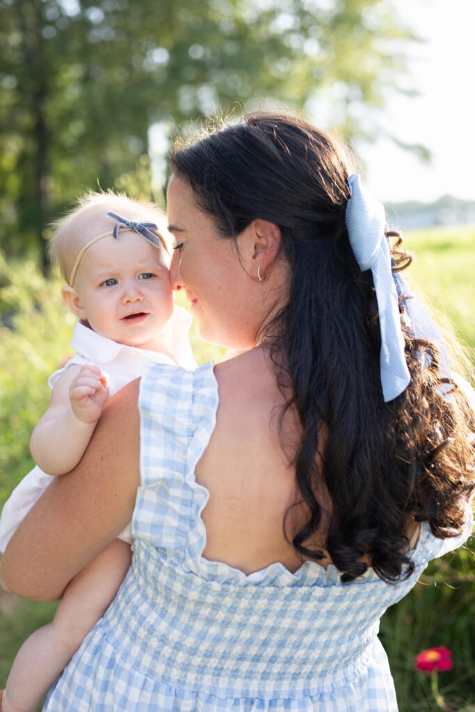 Mom with a Blue bow in her hair holds her baby daughter close and nuzzles her cheek with her nose by Mary Eleanor Photography