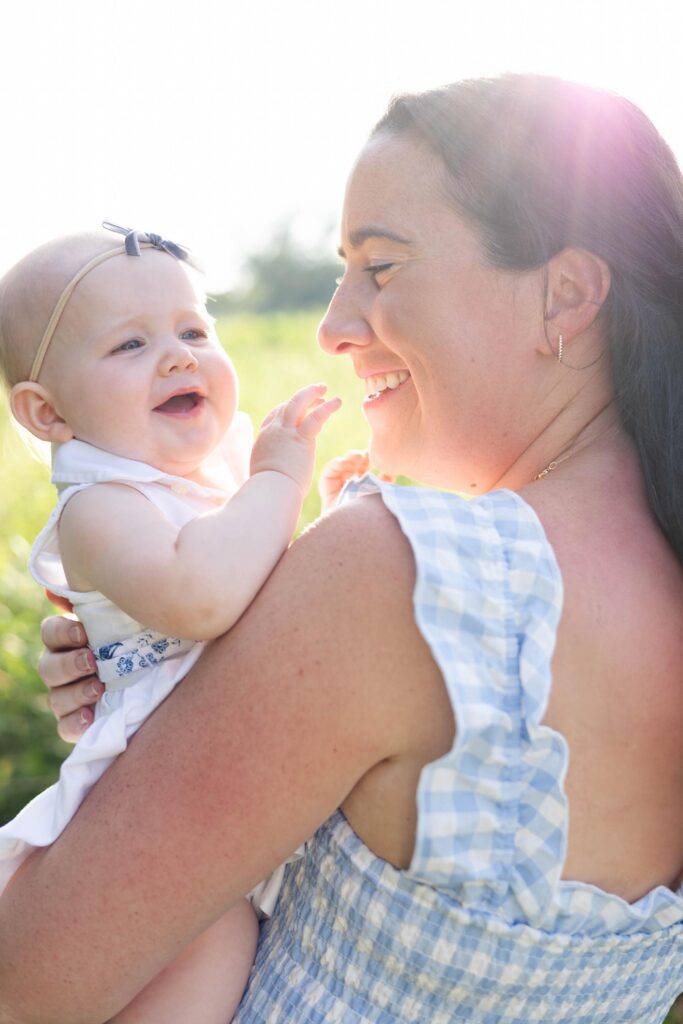 Mom in Blue Gingham dress snuggles her baby daughter close and smiles at her while baby laughs by Mary Eleanor Photography