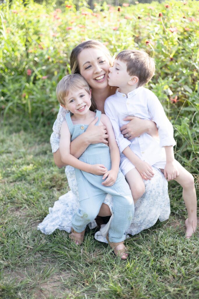 A mom holds her two little boys close while one kisses her cheek and the other smiles at the camera at a Virginia Beach Playground by Mary Eleanor Photography.