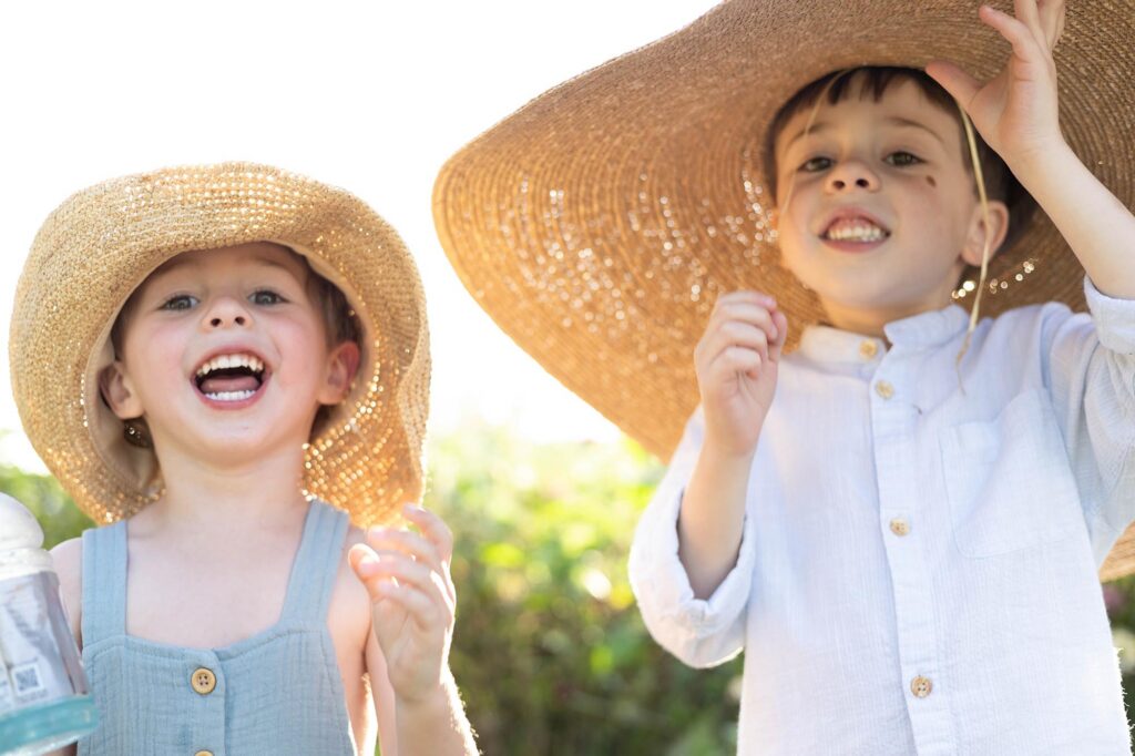 Two little boys laugh while wearing sun hats during a family session By Mary Eleanor Photography.