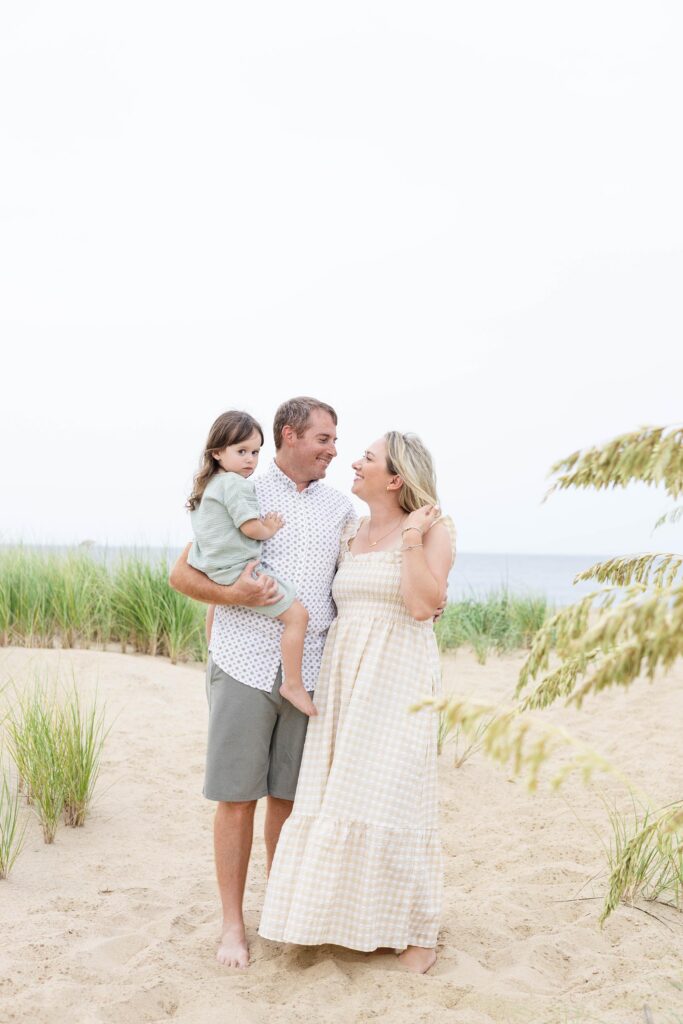 A couple on the Beach during Family photos Virginia Beach snuggle close and while dad holds their shy, snugly toddler.