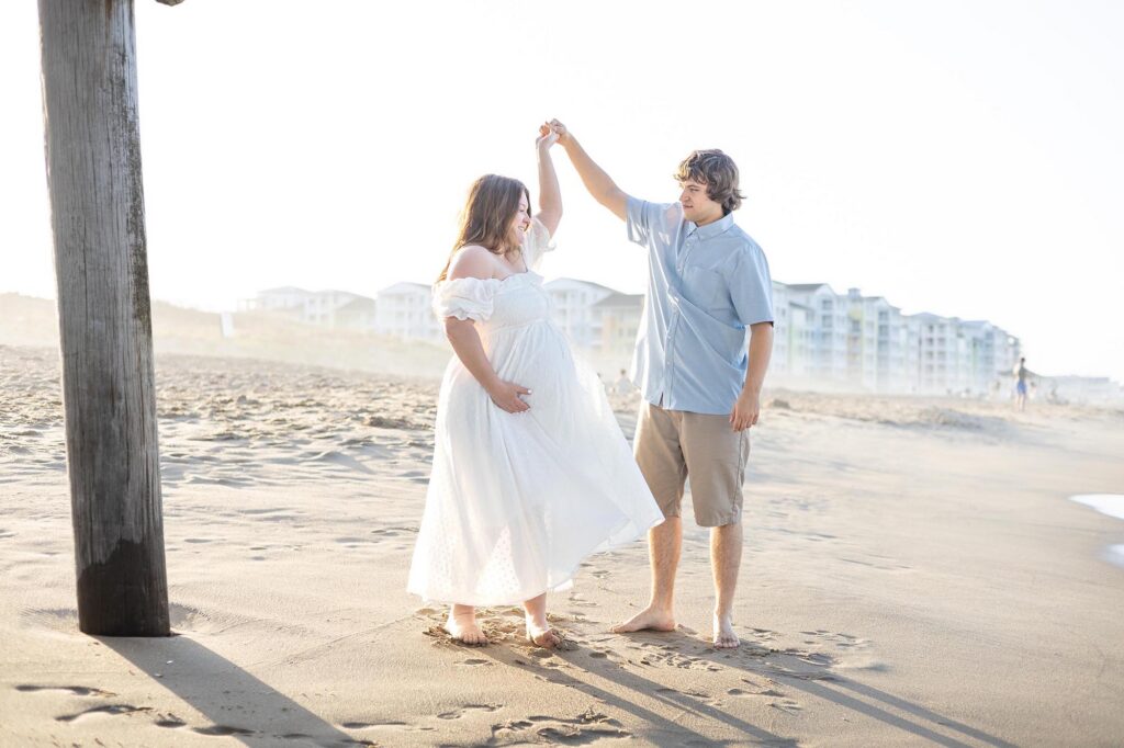 A pregnant woman and her husband  dance together on the beach during a Family Photos Virginia Beach 