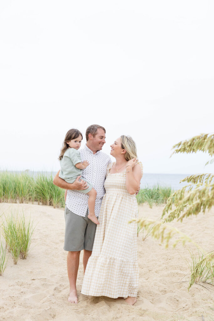 A Family of Three stands on the beach amongst the coastal grasses.