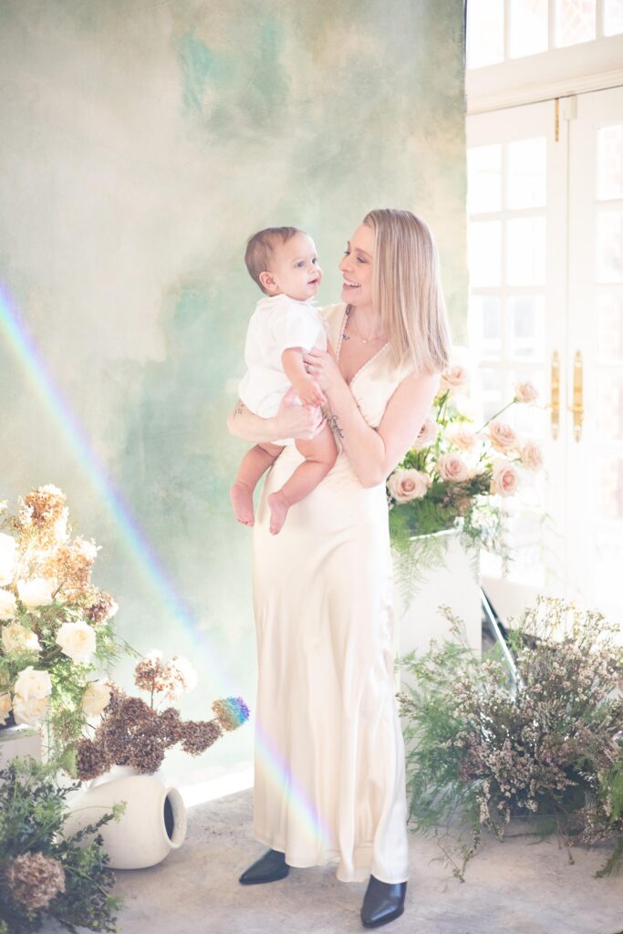 A Mom holds her baby smiling and snuggling while wearing a silk skirt and top set during family photos by Mary Eleanor Photography.