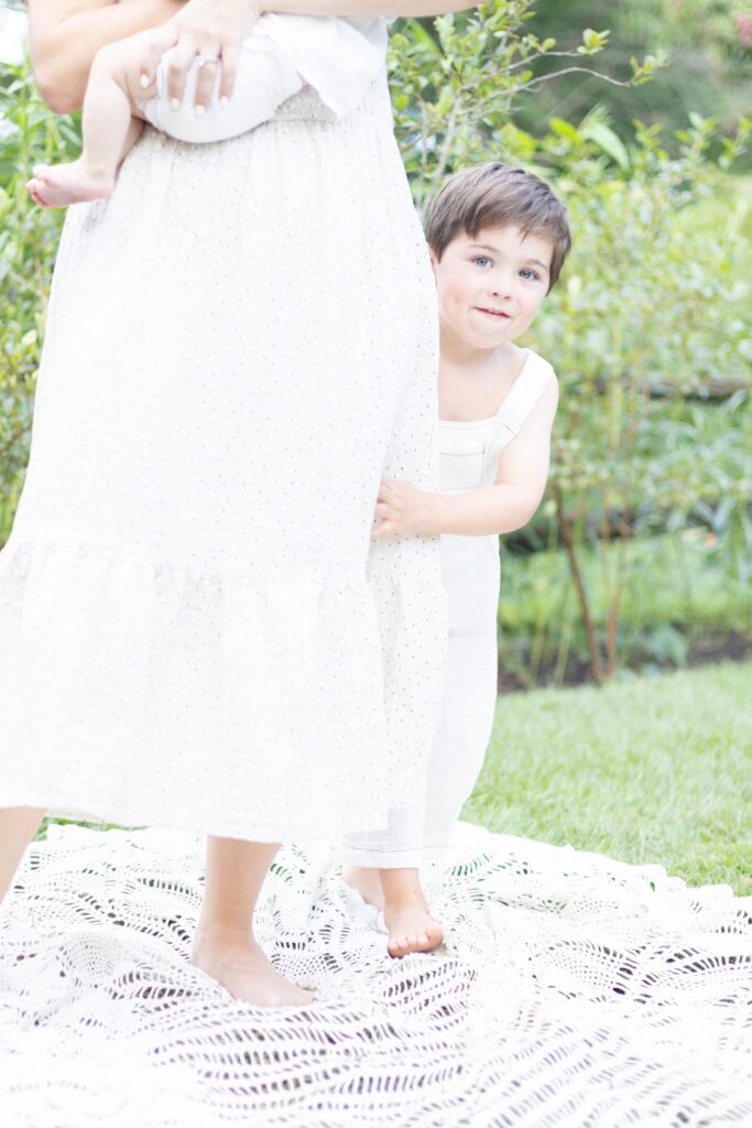 Little boy peeks out from behind his mother's dress during family photos.