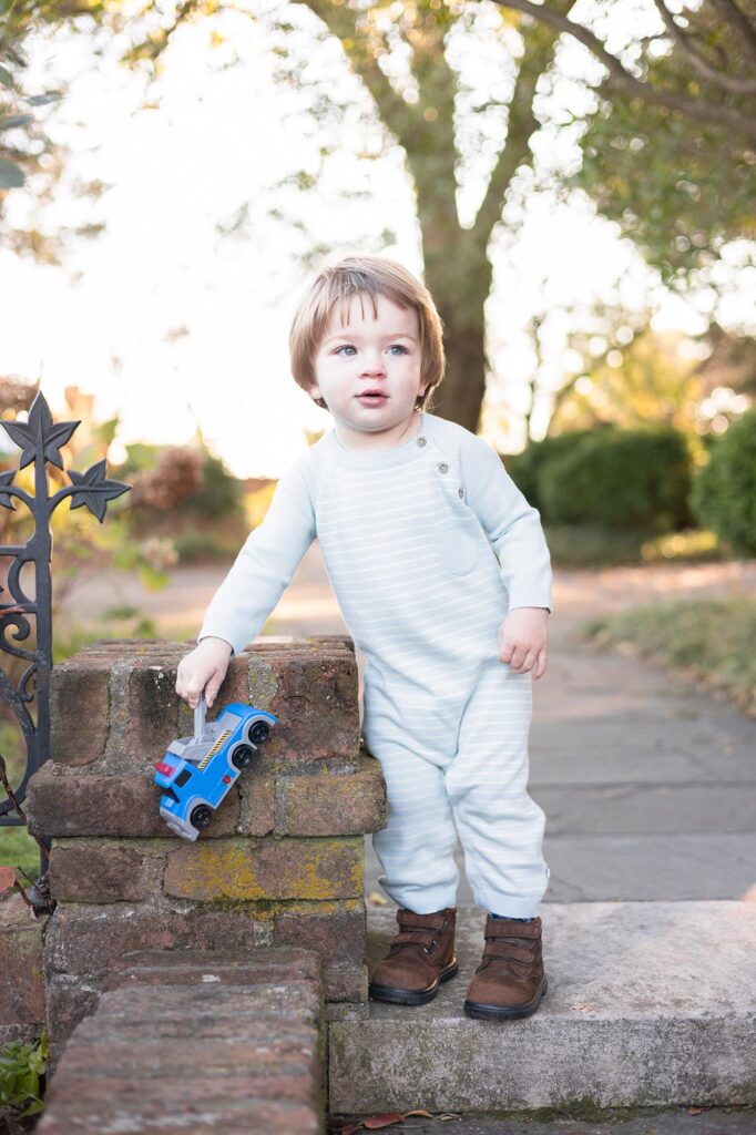 A little boy looks away from the camera while smiling and driving a small toy truck during Fall Family Photos in Virginia Beach.
