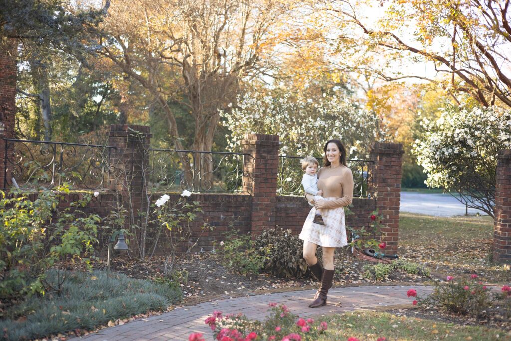 A Mom carries her toddler son through a Fall garden during Fall Family Photos in Virginia Beach by Mary Eleanor Photography.