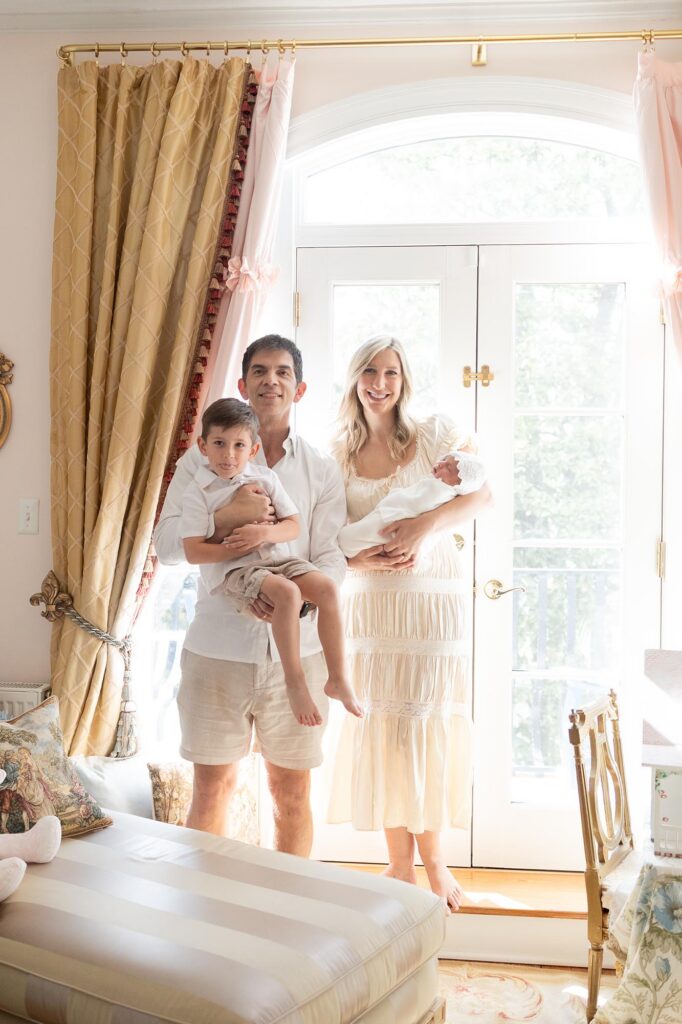 Dad holds toddler while mom cradles newborn baby during in-home newborn photos with siblings.