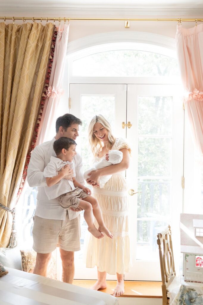 Dad and toddler look at mom and newborn sibling during in-home newborn photos with siblings.